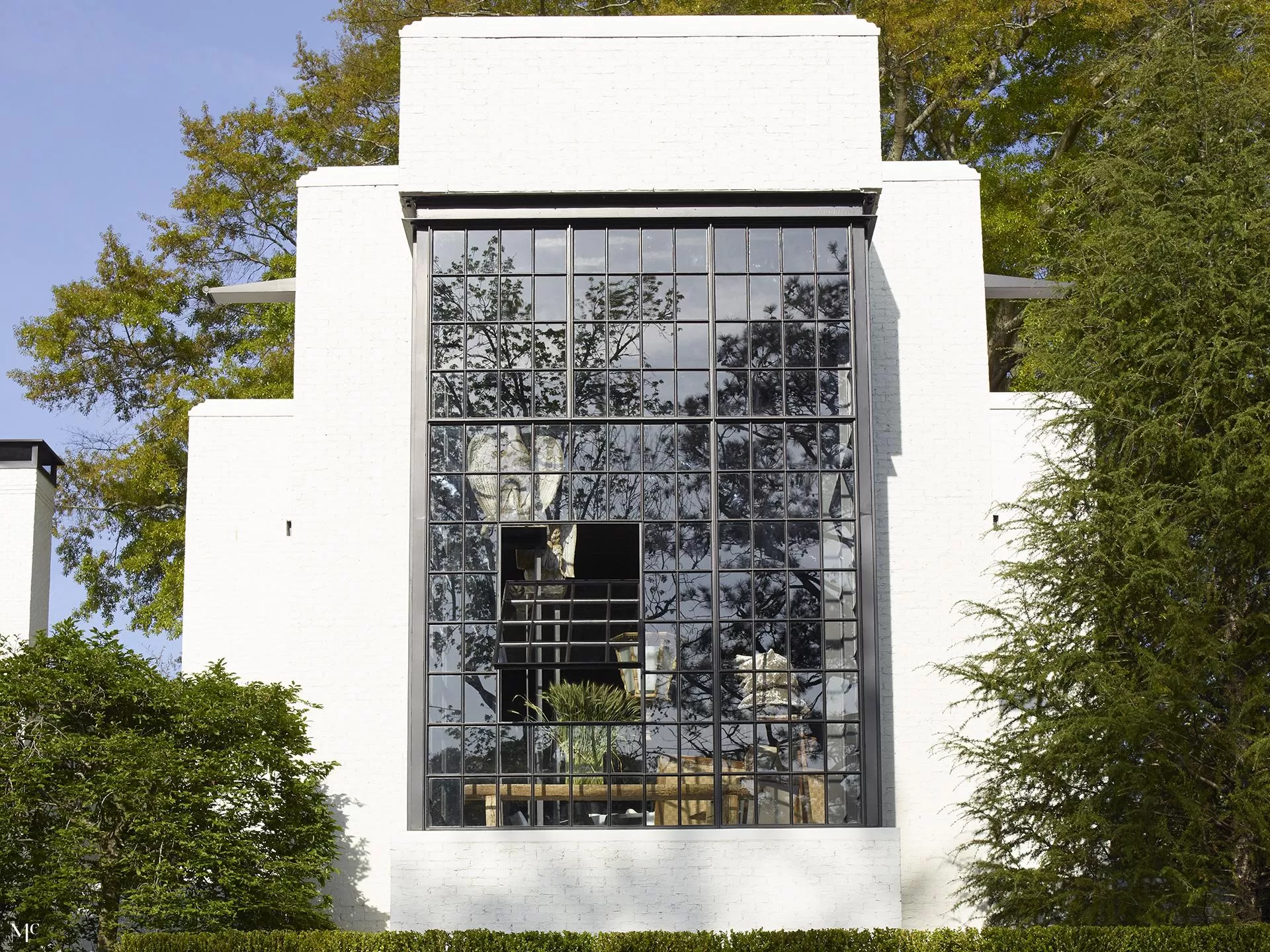 A large modern window facade reflecting trees and sky, framed by a white brick exterior.