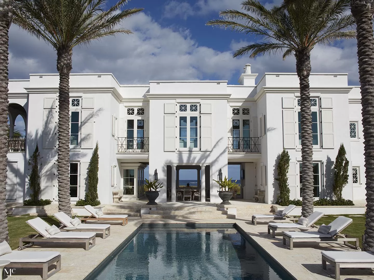 A white beach house exterior with palm trees of both sides of the entrance.