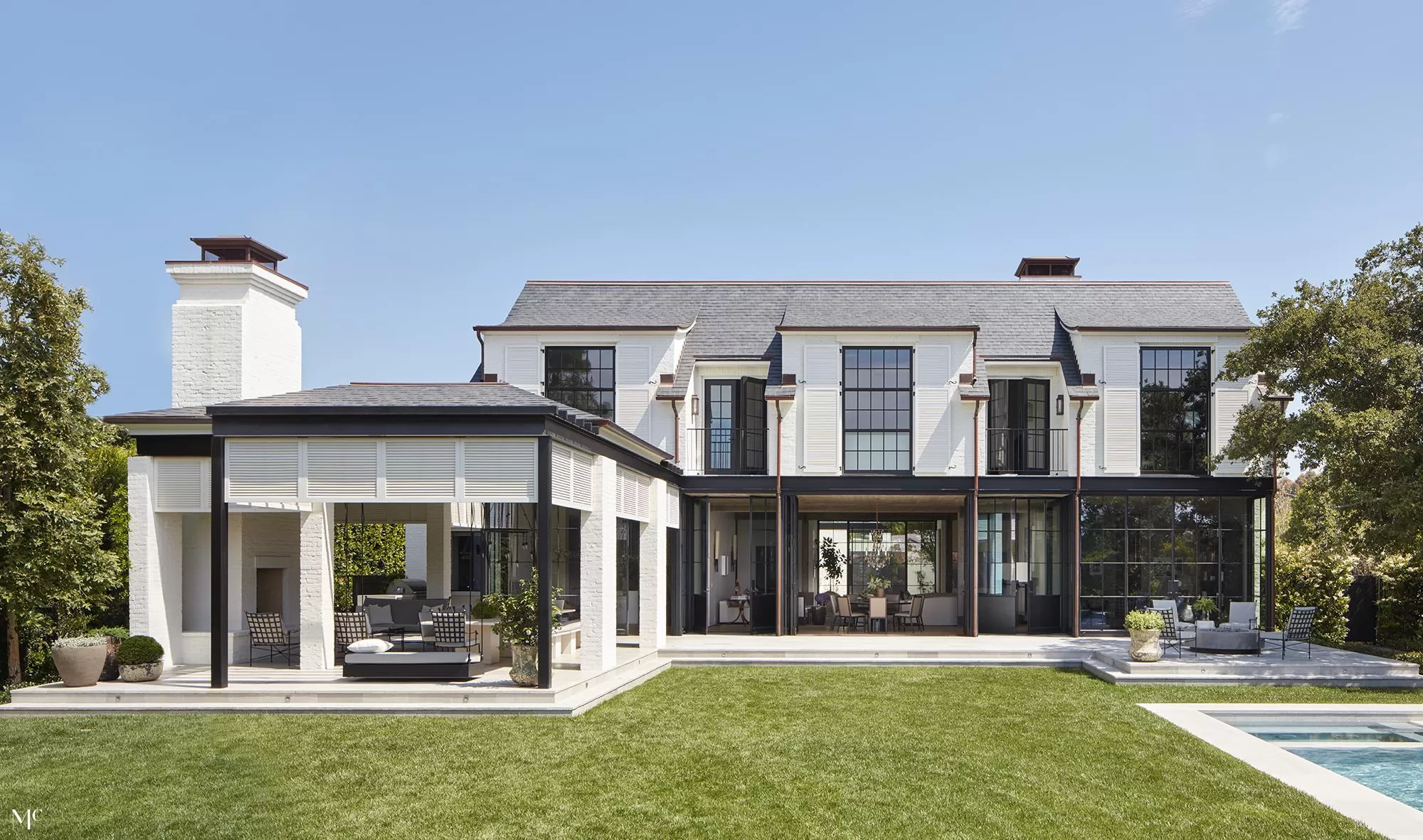 An architectural front view of a modern farmhouse courtyard with white and black buildings, large glass doors, oversized trees, and neutral tones