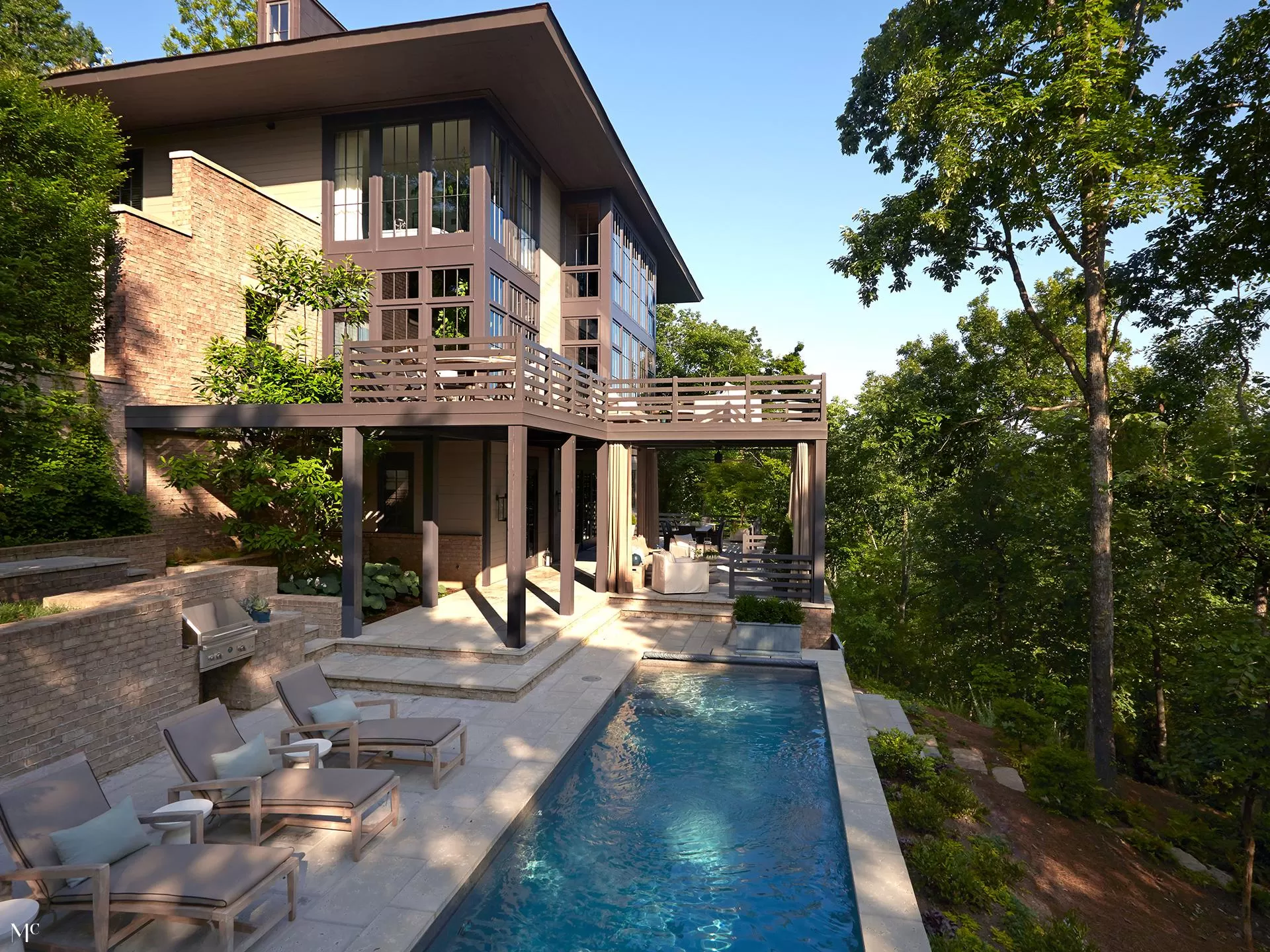 A modern, two-story home with a large outdoor patio and pool, in the style of modernist architecture, overlooking lush green trees