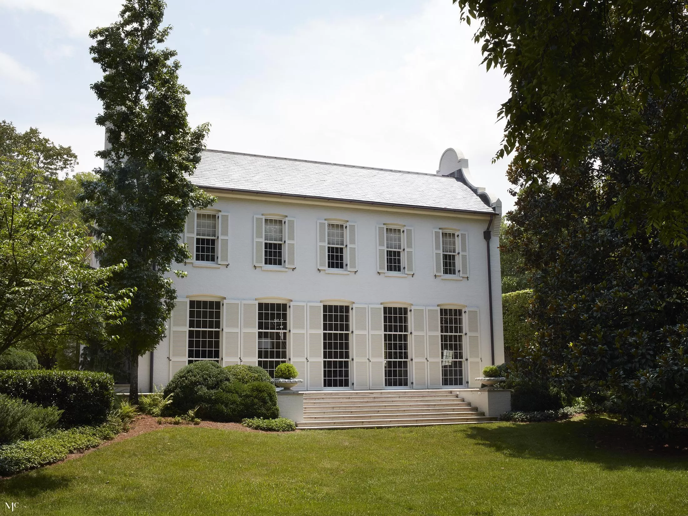 A large white house with double windows and shutters in the front yard