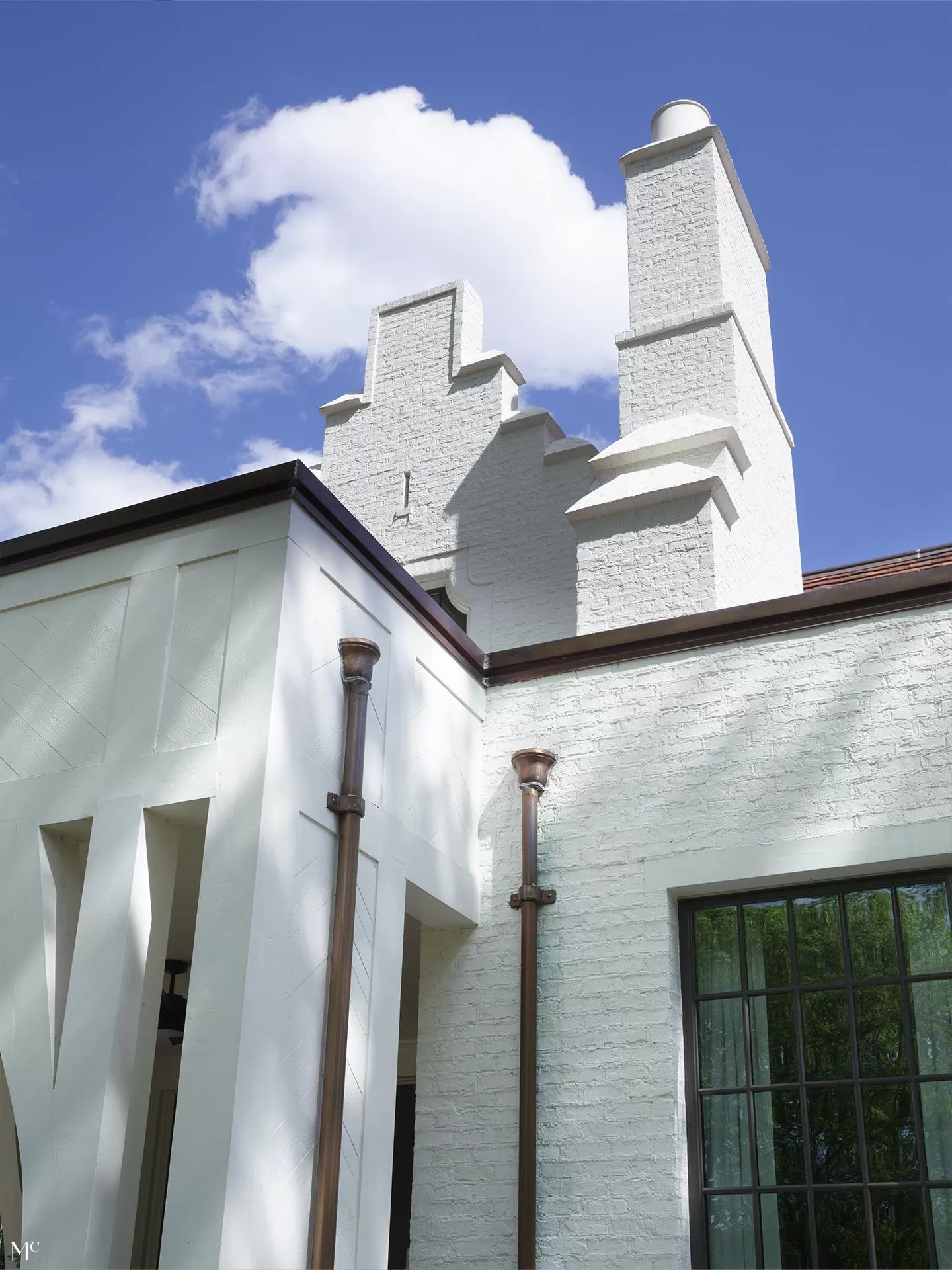 A white brick house with a large chimney, a dark brown pipe sleeve on the side of the home