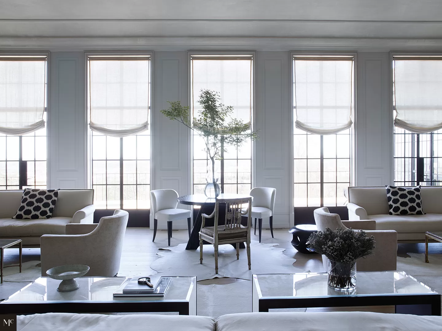 A large living room with white walls, black and silver accents, a dining table in the center of an all-white space