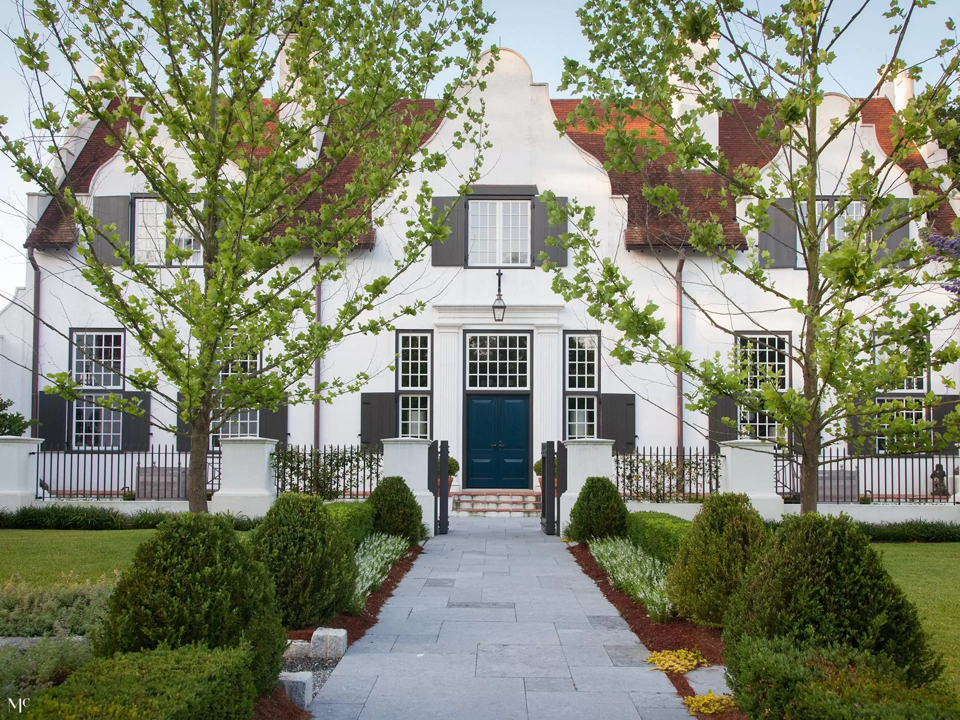 classic colonial-style white house with black shutters, front view, blue door, and large trees in the yard, with navy-blue details, white walls, and a symmetrical design