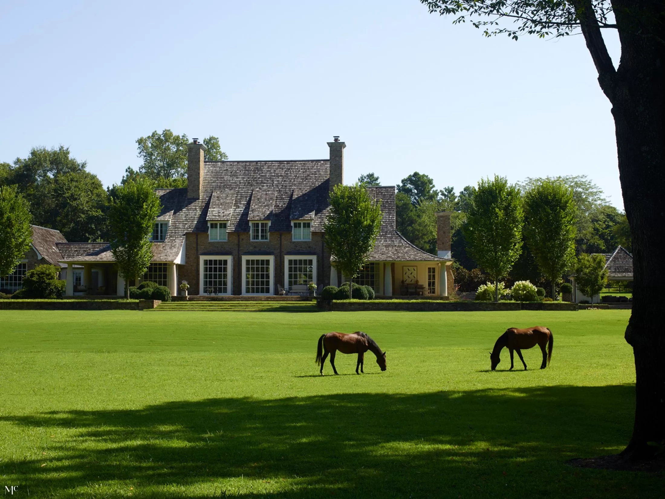 A large colonial-style home with horses grazing on the front lawn