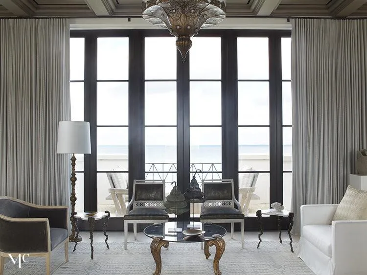 Floor to ceiling windows looking out to the ocean, with black and white simple furniture designs.