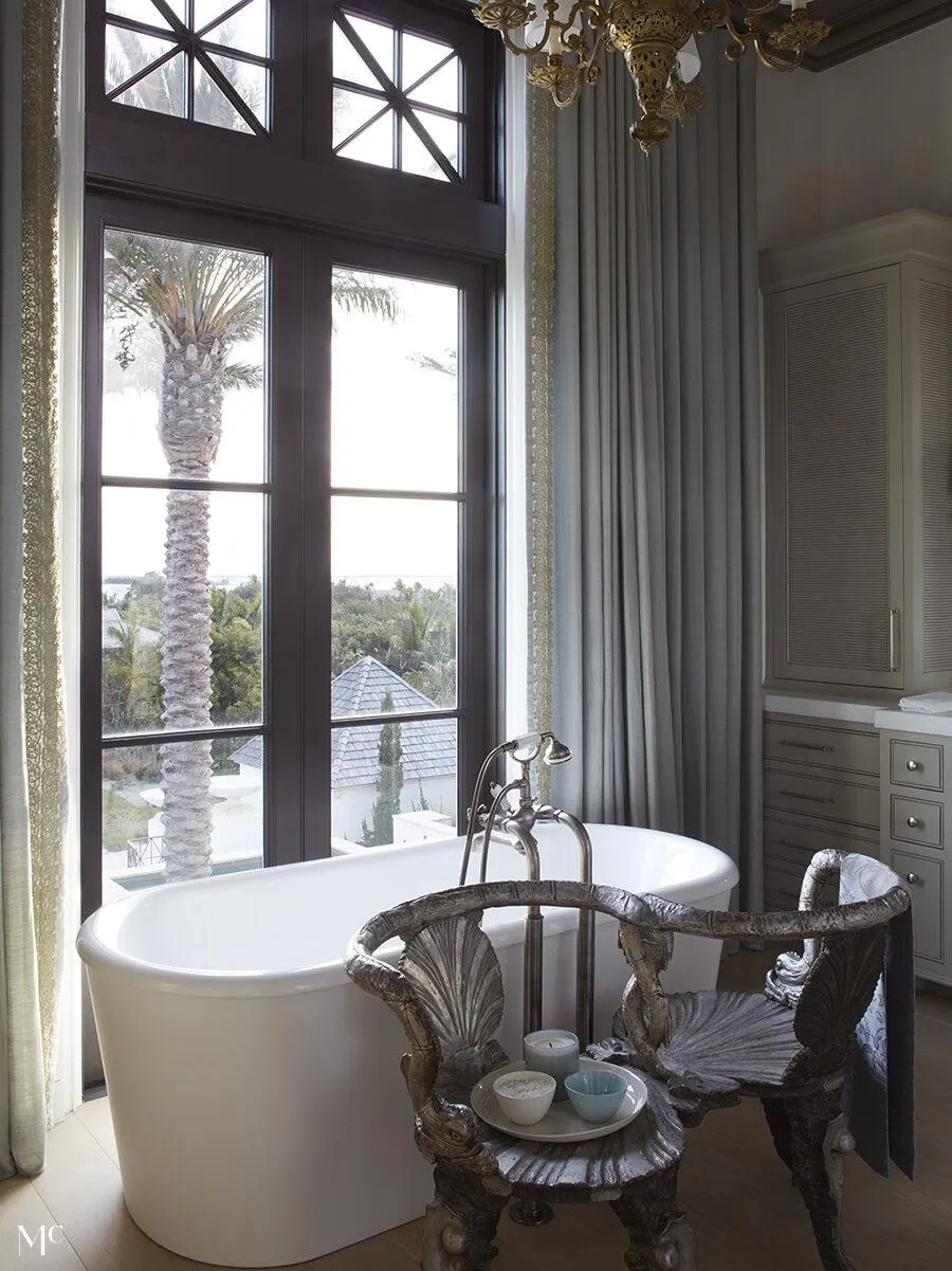 Bathtub outlooking into palm trees with neutral palette walls and deco