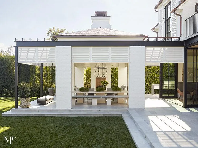 An architectural back view of a modern farmhouse courtyard with white and black buildings, large glass doors, oversized trees, and neutral tones