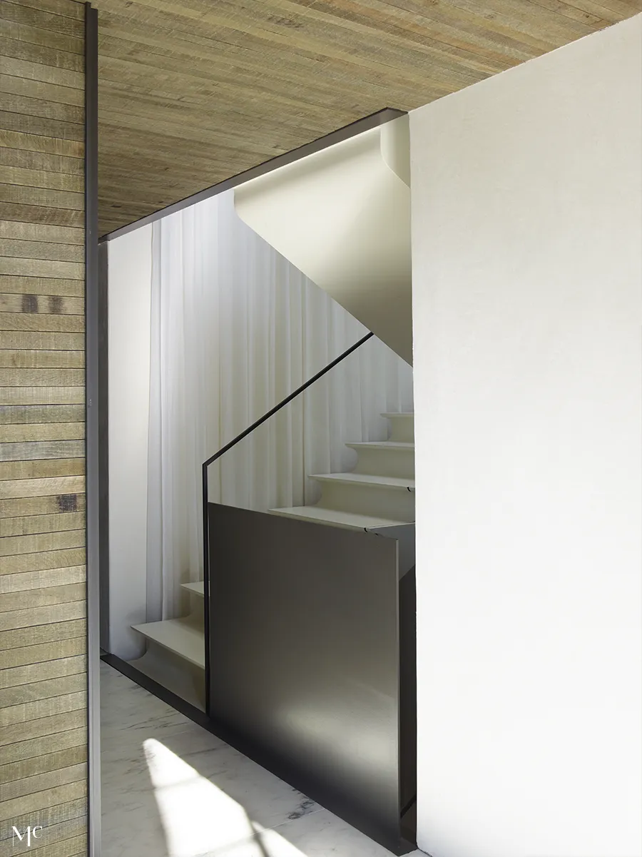 A minimalist staircase with white walls, wood slats, black metal details, and natural light