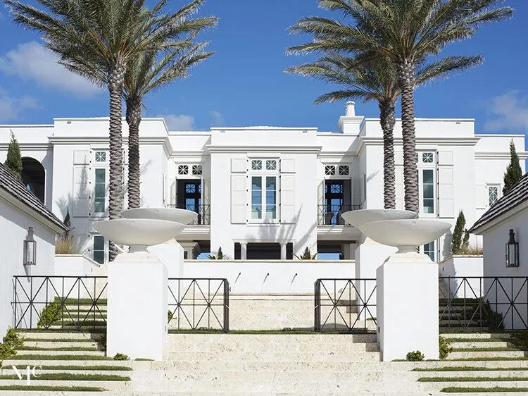 A white beach house exterior with palm trees of both sides of the entrance.