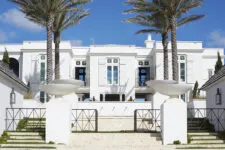 A white beach house exterior with palm trees of both sides of the entrance.