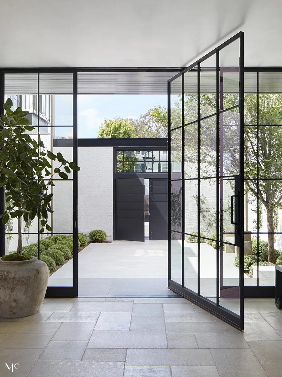 Entrance of a house with large glass doors leading to greeneries