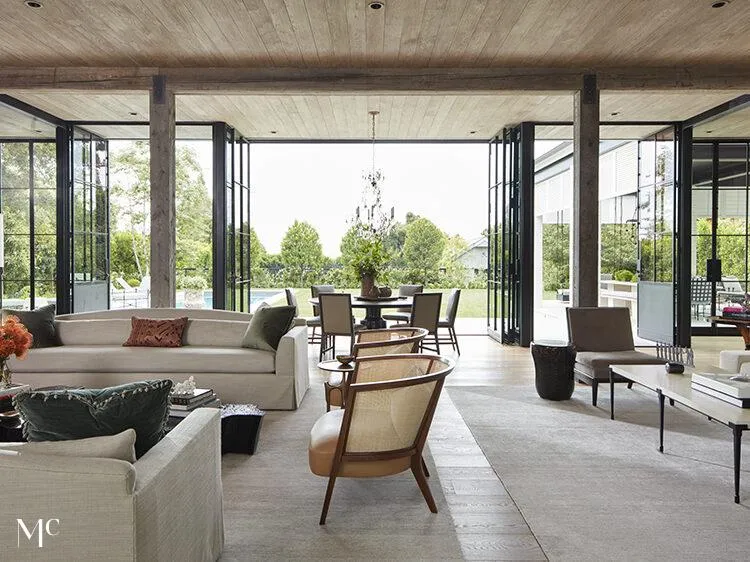 living room with large glass doors leading to an outdoor dining area, featuring modern neutral-toned furniture, and natural light