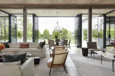 living room with large glass doors leading to an outdoor dining area, featuring modern neutral-toned furniture, and natural light