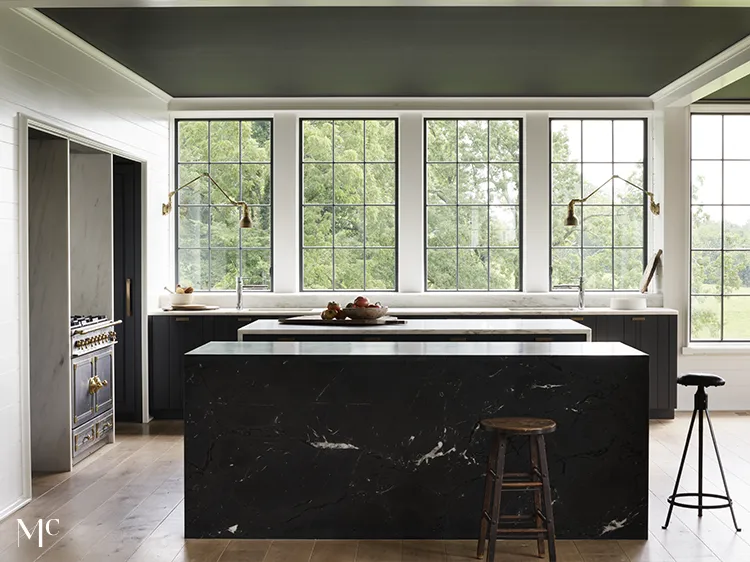 white and wood kitchen with black countertops and large windows overlooking woods