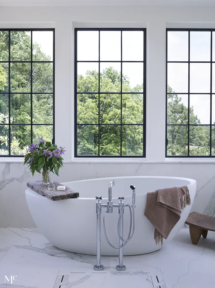 white marble interiors with white bathtub and large windows outlooking trees