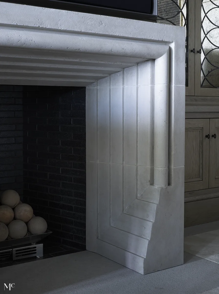 A close-up photo of an elegant fireplace made from white stone with silver accents.