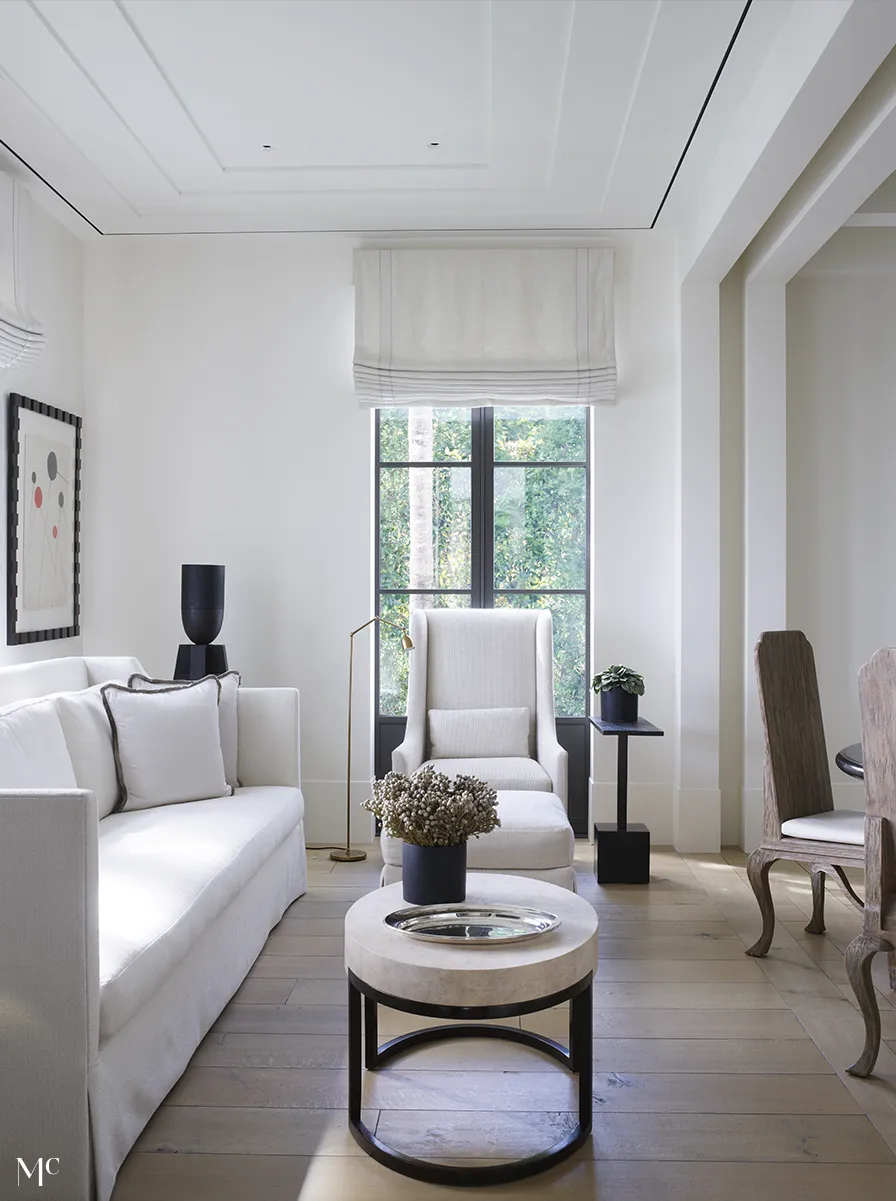 Living room with light wood floors, tall windows, and white walls and white furniture