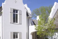 White brick and shingle ornate house with a tall gable roof, fluted window details, stone accents