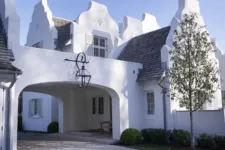 White brick and shingle ornate house with a tall gable roof, fluted window details, stone accents