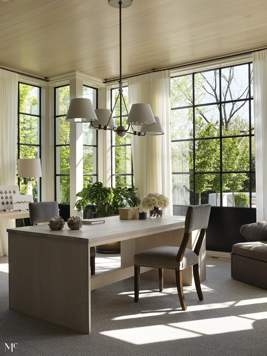 neutral wood tones in a dining room with large floor to ceiling windows looking out to the lawn and trees