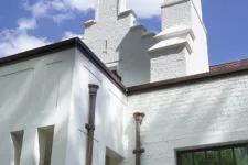 A white brick house with a large chimney, a dark brown pipe sleeve on the side of the home