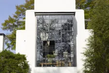 A large modern window facade reflecting trees and sky, framed by a white brick exterior.