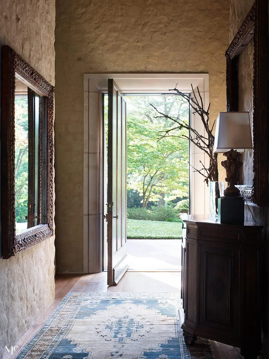 rustic entryway with an open door leading to the garden, framed by antique mirrors and vintage-inspired sideboards