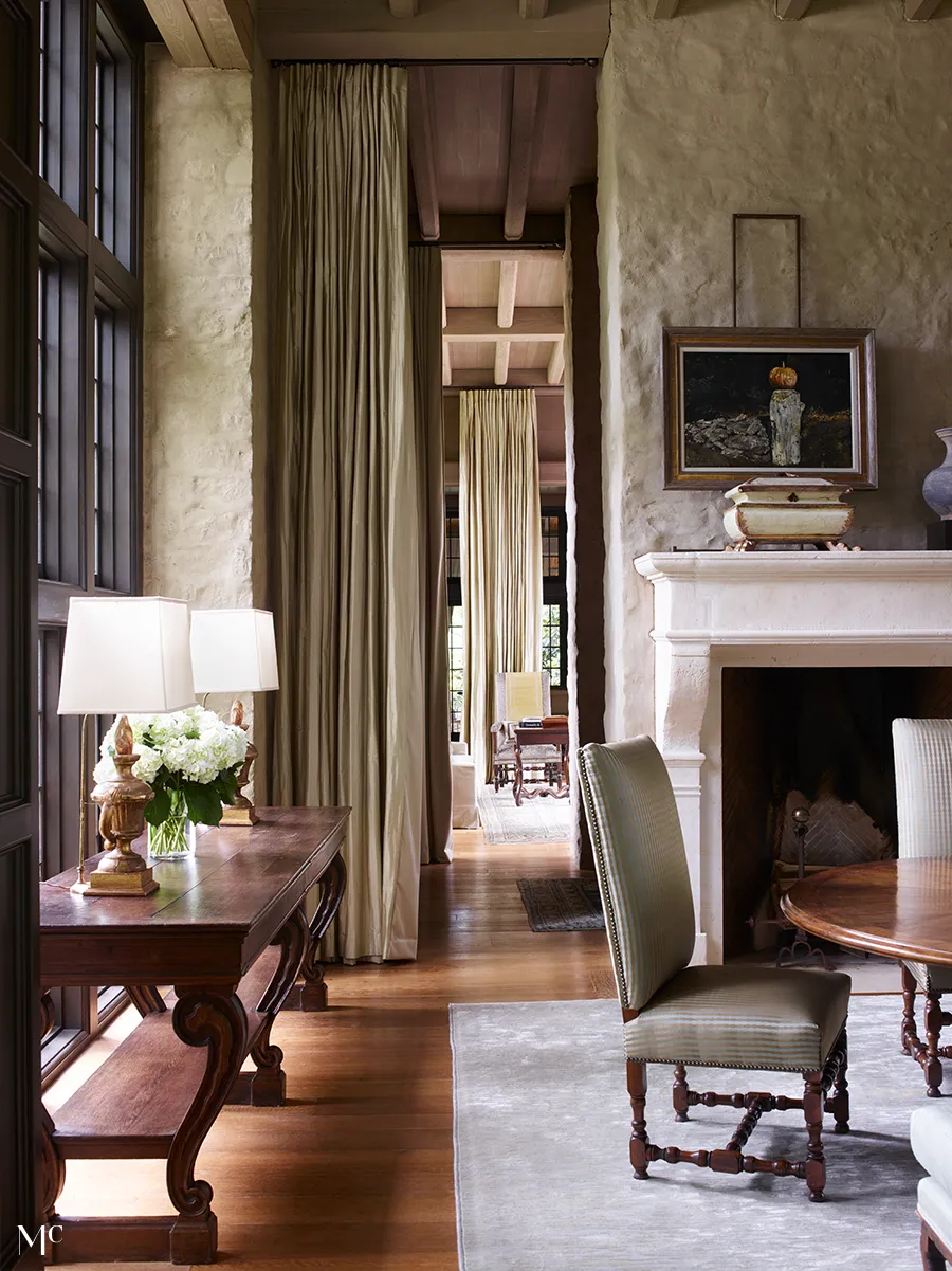 elegant home office with long curtains, fireplace and dining table in the style of tuscany stone walls and cream colored linen drapes