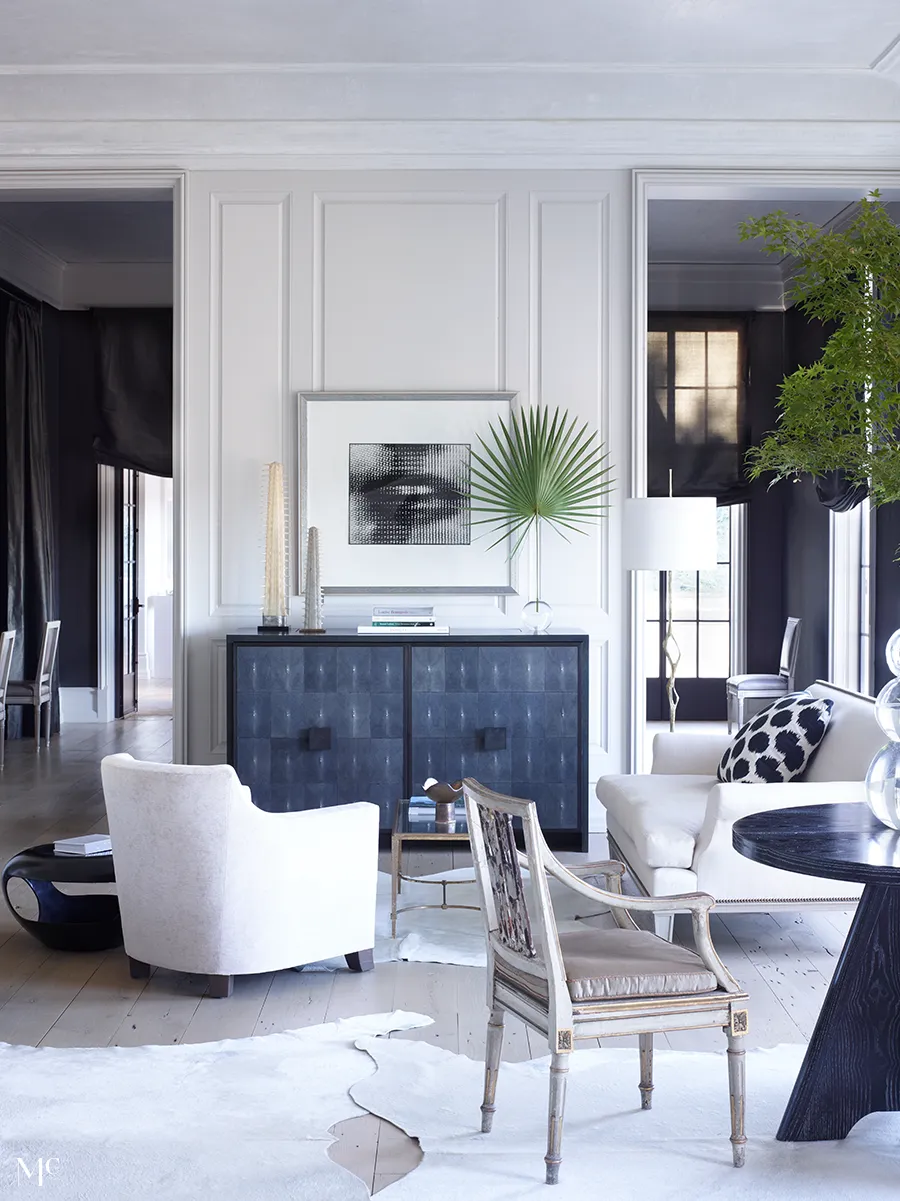 A large living room with white walls, black and silver accents, a dining table in the center of an all-white space