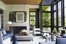 A modern farmhouse-style living room with a fireplace, blue accents, and large windows