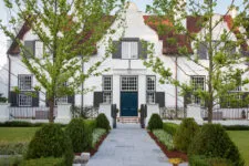 classic colonial-style white house with black shutters, front view, blue door, and large trees in the yard, with navy-blue details, white walls, and a symmetrical design