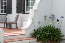 classic colonial-style white house with black shutters, front view, blue door, and large trees in the yard, with navy-blue details, white walls