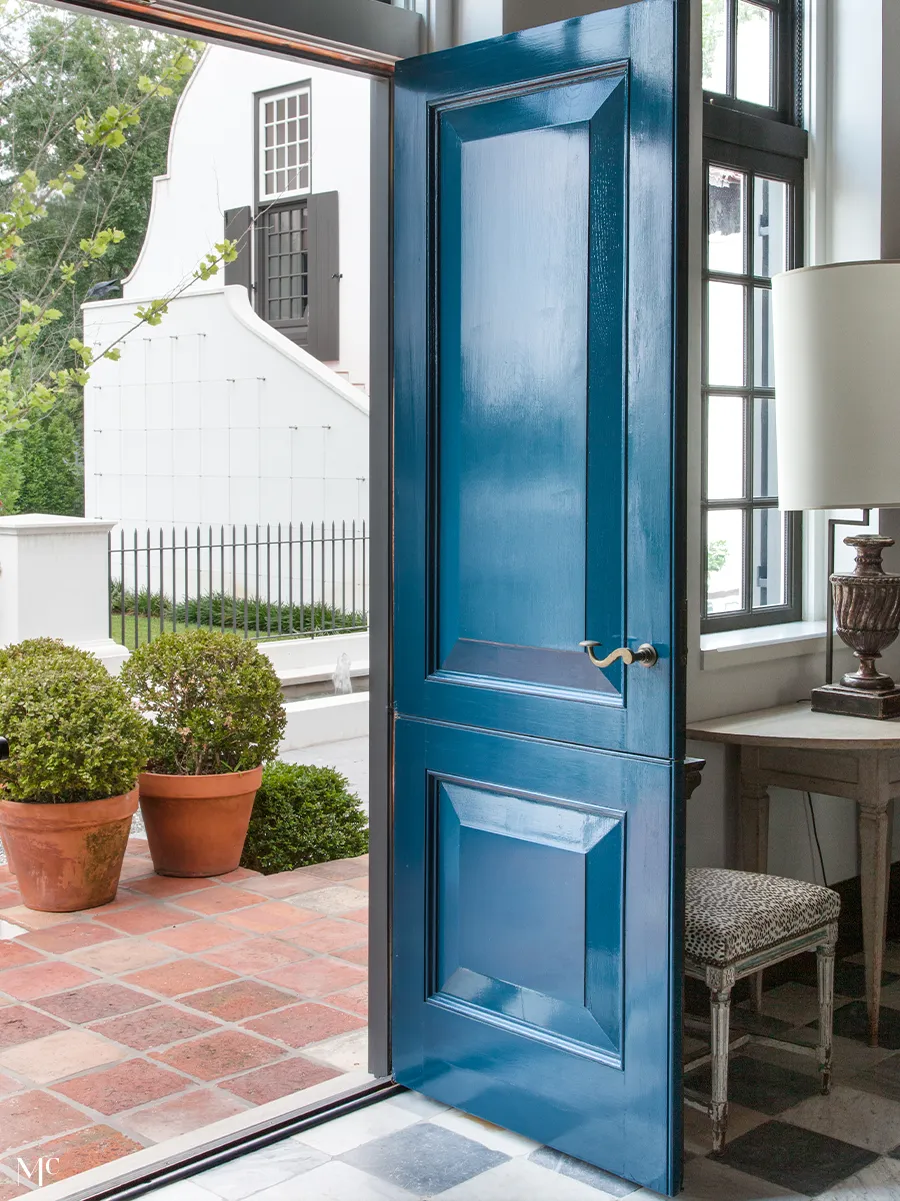 classic colonial-style white house with black shutters, front view, blue door, and large trees in the yard, with navy-blue details, white walls and blue door