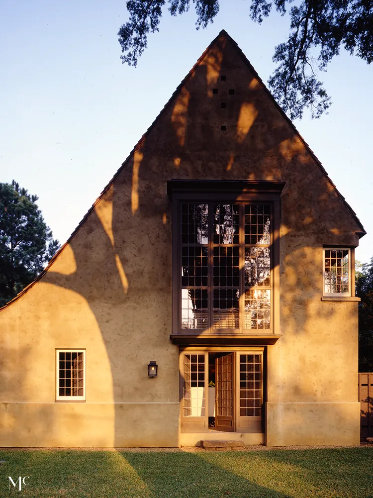 back view of an old, rustic cottage with a gray shingle roof surrounded by stone walls