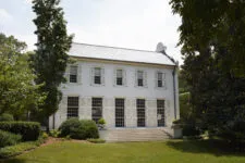 A large white house with double windows and shutters in the front yard